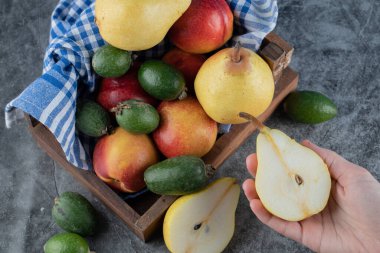 Taze meyve sepetinin en üst görüntüsü. Yarısı kesilmiş armut tutan bir kadın.