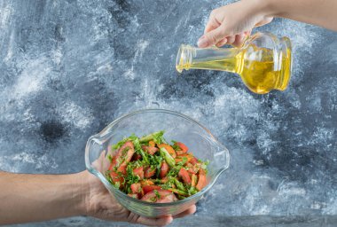 El sebze salatasına yağ döküyor.