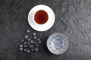 Lezzetli taze yaban mersinli seramik kase ve siyah yüzeyde bir fincan çay.