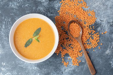 Tahta kaşıklı beyaz bir kâse mercimek çorbası.