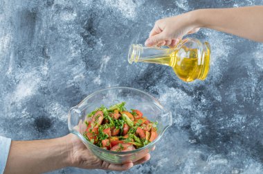 El sebze salatasına yağ döküyor.