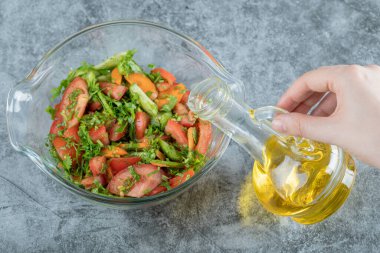 El sebze salatasına yağ döküyor.