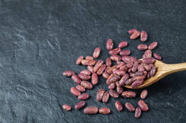 Koyu arka planda bir avuç çiğ fasulye ve tahta kaşık.