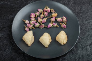 Kurumuş gül ve hamur işleriyle dolu siyah bir tabak.