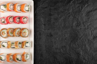 Siyah masada değişik lezzetli suşi çeşitleri olan beyaz bir tahta.