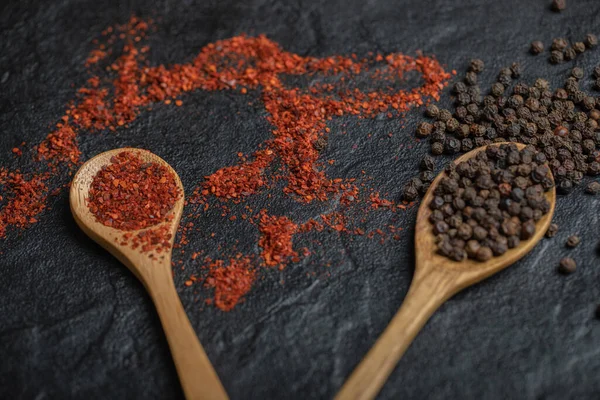 Red and black peppercorns with wooden spoon over black background
