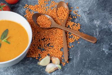 Beyaz bir kase mercimek çorbası, domatesli ve tahta kaşıklı.