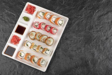 Siyah masada değişik lezzetli suşi çeşitleri olan beyaz bir tahta.