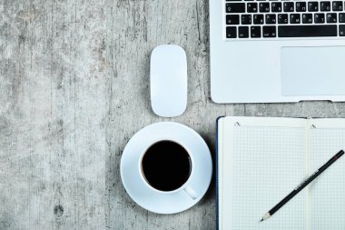 Not defteri, dizüstü bilgisayar, fare ve ahşap masada bir fincan çay.