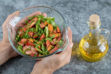 Kadın elleri mermer arka planda sebze salatası kasesi tutuyor.