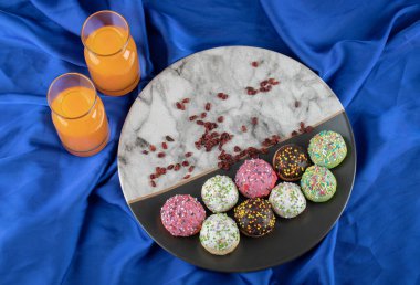 Mavi kumaş üzerinde portakal suyu ve bir tabak renkli kurabiye.