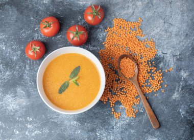 Beyaz bir kase mercimek çorbası, domatesli ve tahta kaşıklı.