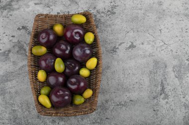 Taştan arkaplanda taze mor erikler olan hasır bir sepet.