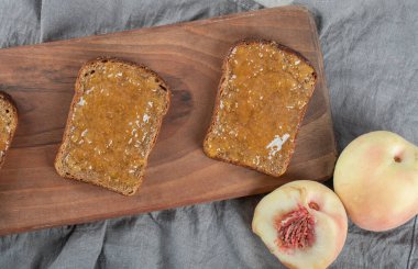 Tahta kesme tahtasının üzerinde şeftali reçelli kahverengi ekmek dilimleri