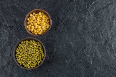 İki kase dolusu yeşil zeytin ve siyah arka planda mısır tohumu.