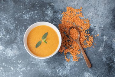 Tahta kaşıklı beyaz bir kâse mercimek çorbası.