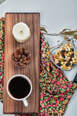 Bir fincan mumlu kahve, orman konisi, tahtanın üzerinde fındıklar.