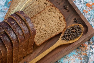 Tahtada taze ekmek dilimleri ve kaşık dolusu biber taneleri.