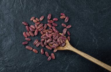 Koyu arka planda bir avuç çiğ fasulye ve tahta kaşık.