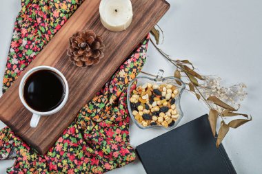 Bir fincan mumlu kahve, orman konisi, tahtanın üzerinde fındıklar.