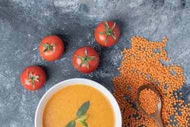 Beyaz bir kase mercimek çorbası, domatesli ve tahta kaşıklı.