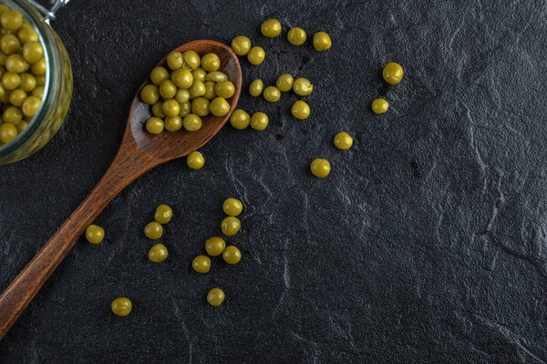 Маринованные зеленые оливки с деревянной ложкой на черном фоне