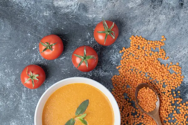 Beyaz bir kase mercimek çorbası, domatesli ve tahta kaşıklı.