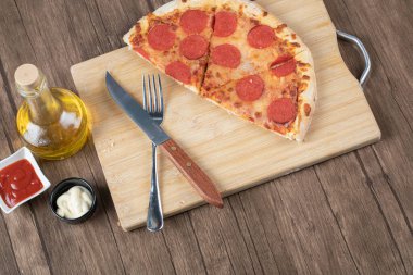 Biberli pizzanın yarısı ahşap tabakta soslu ve yağlı.