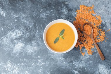 Tahta kaşıklı beyaz bir kâse mercimek çorbası.