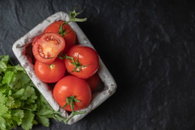 Taze olgun domateslerin sepet ve kişniş yapraklarının üst görüntüsü.