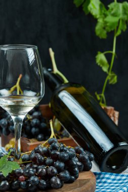 Bir bardak şarap ve siyah arka planda bir şişe siyah üzüm.