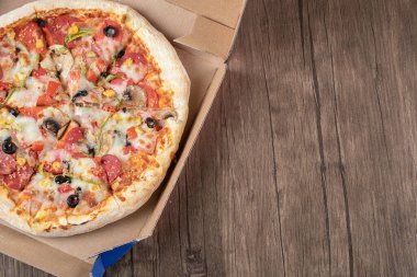 Pizza kutusundaki taze karışık pizzanın ahşap arka planda üst görüntüsü.