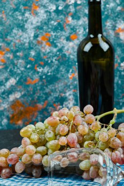 Taze kırmızı üzüm ve mavi arka planda şarap şişesi.