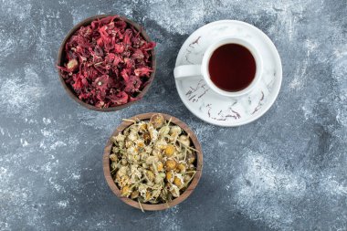 Bir fincan çay ve mermer arka planda iki kase kurutulmuş çiçek.