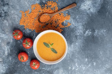 Beyaz bir kase mercimek çorbası, domatesli ve tahta kaşıklı.