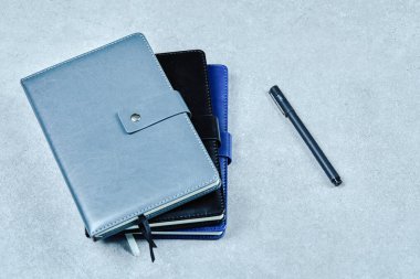 Mavi arka planda üç defter ve bir kalem. Düz yatıyordu