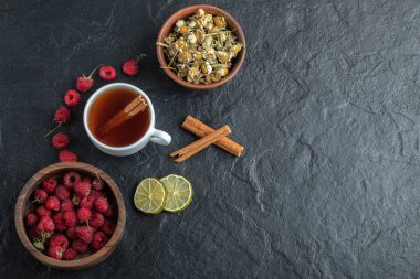 Taze ahududu ve siyah arkaplanda papatya çayı.