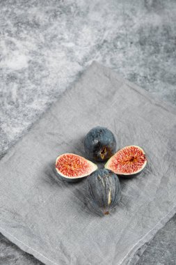 Mermer bir arka planda gri masa örtüsü olan olgun, lezzetli incirler.