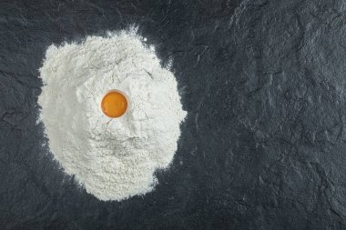 Gri arkaplanda çiğ yumurta sarısı olan un.