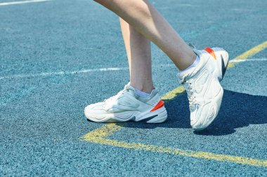 Mavi arka planda beyaz spor ayakkabı giyen bir kadın.