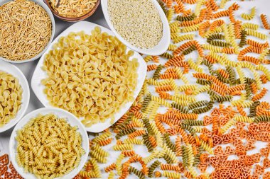 Renkli, dağınık fusilli ve beyaz arka planda çiğ makarna kaseleri.