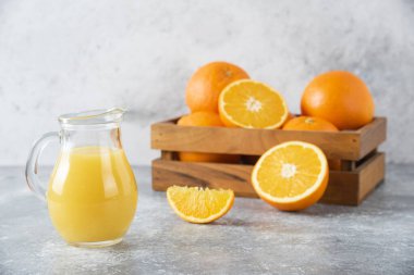 Taş zemin üzerinde taze portakal meyveleri olan cam bir sürahi meyve suyu. Yüksek kalite fotoğraf