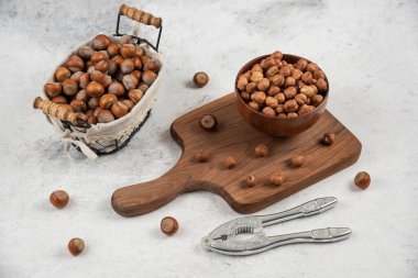 Bir sepet kabuklu fındık, çekirdek ve fındık kırma aleti kesme tahtasının yanında.