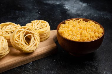 Erişte ahşap bir tahtanın üzerinde yuvarlanıyor ve makarna çeşitleri tahta bardaklarda.