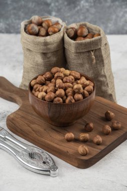 Bir kase organik fındık çekirdeği kabuklu fındık dilimlenmiş tahtanın üzerinde.