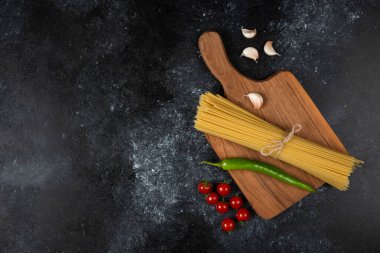 Biberli spagettiler, domatesler ve sarımsaklar tahtanın üzerinde.