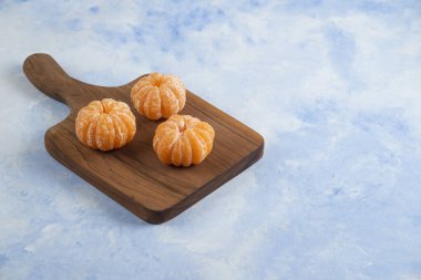 Ahşap kesme tahtasının üzerinde üç taze soyulmuş mandalina. Fotoğrafı kapat.