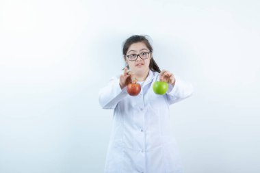 Doktor üniformalı genç bir kız elinde yeşil ve kırmızı elma meyveleri tutuyor. Yüksek kalite fotoğraf