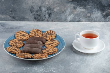 Mavi tabak dolusu çikolatalı kek ve bir fincan sıcak çayla kepekli kurabiye. Yüksek kalite fotoğraf