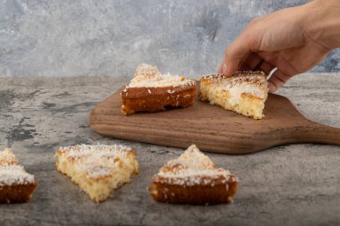 Erkek el, tahta kesme tahtasına yerleştirilmiş hindistan cevizi talaşı ile tatlı dilimini alıyor. Yüksek kalite fotoğraf